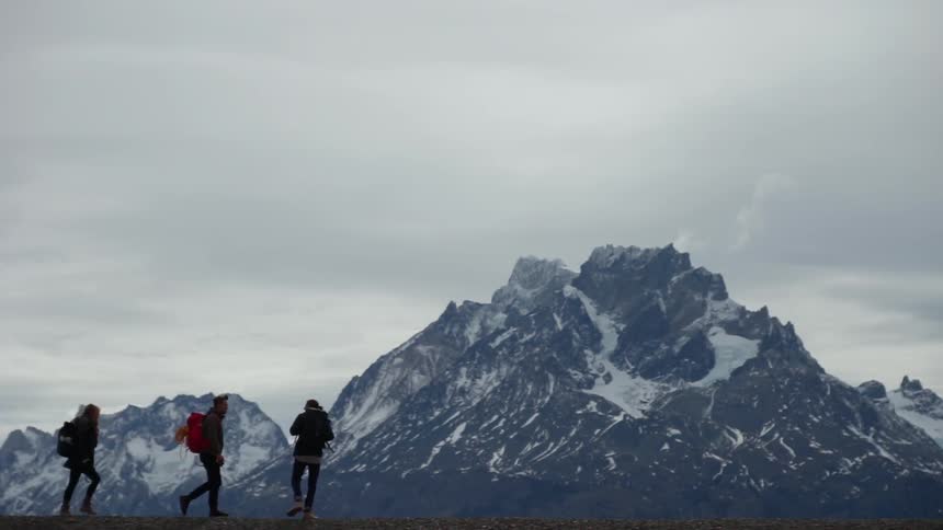 Two people hike past a snow covered mountain