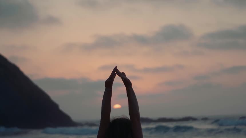 A woman does yoga on a beach at sunset