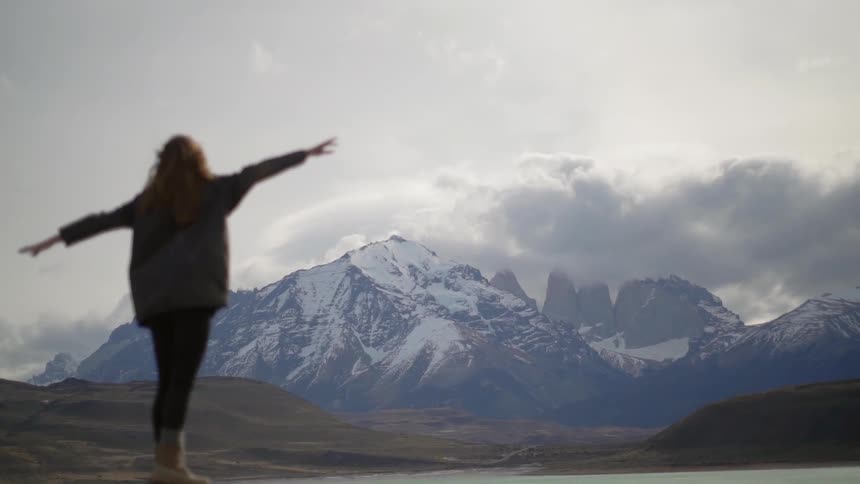 A woman balances on a rock next to a mountain lake