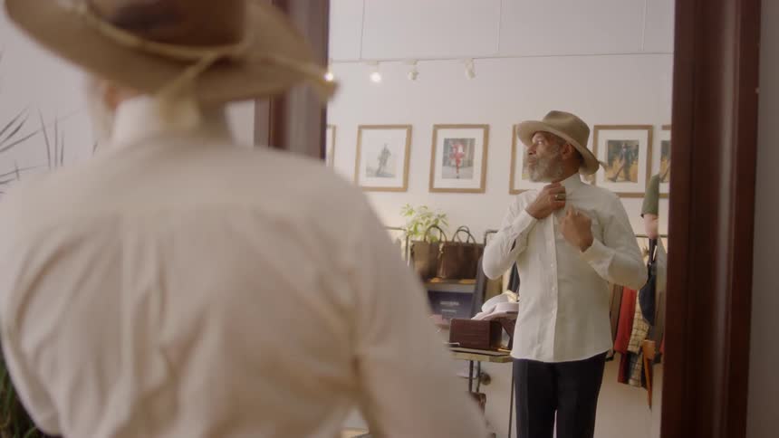 Man buttons a shirt as he stands in front of a mirror at a store
