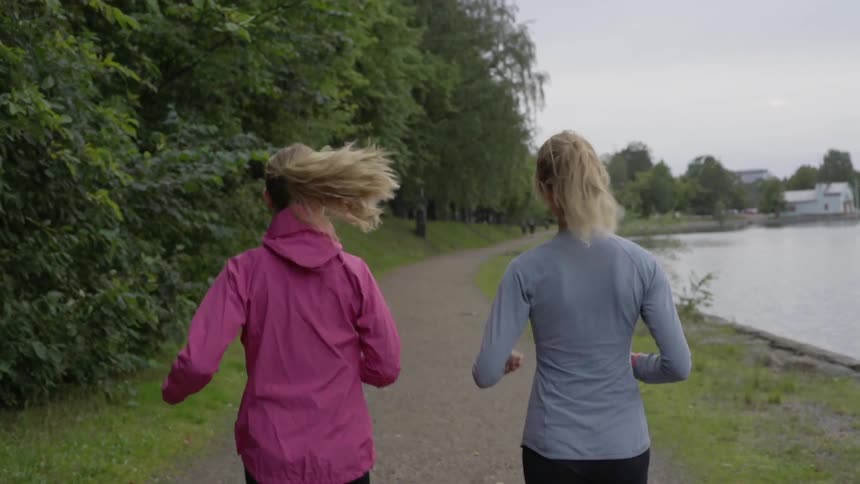 Two runners with ponytails jog together near a lake during an afternoon workout.