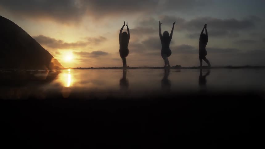 Three people are doing yoga on the beach at dawn