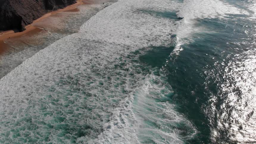 Waves are rolling toward a beach at the base of cliffs during the day