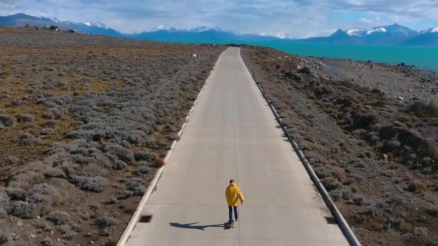 A skateboarder rides on a rural road towards mountains