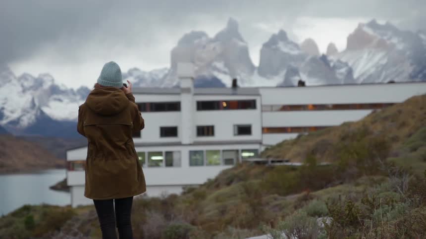 A woman photographs a building near snowy mountains