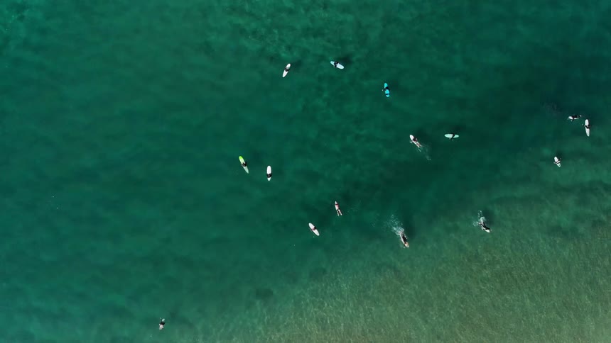 Surfers sit on their boards or paddle further out