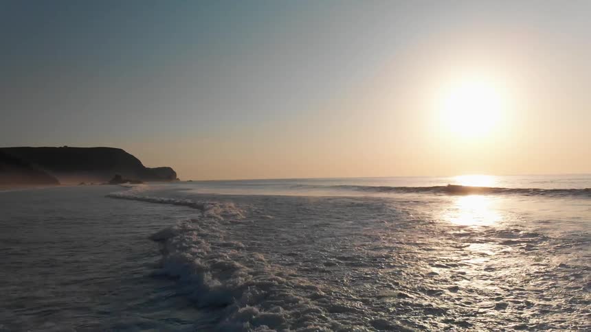 A wave is crashing towards the shore near sunset