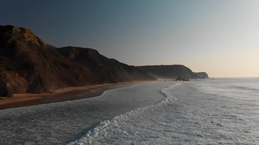 Waves are crashing on the shore with mountains close to the beach