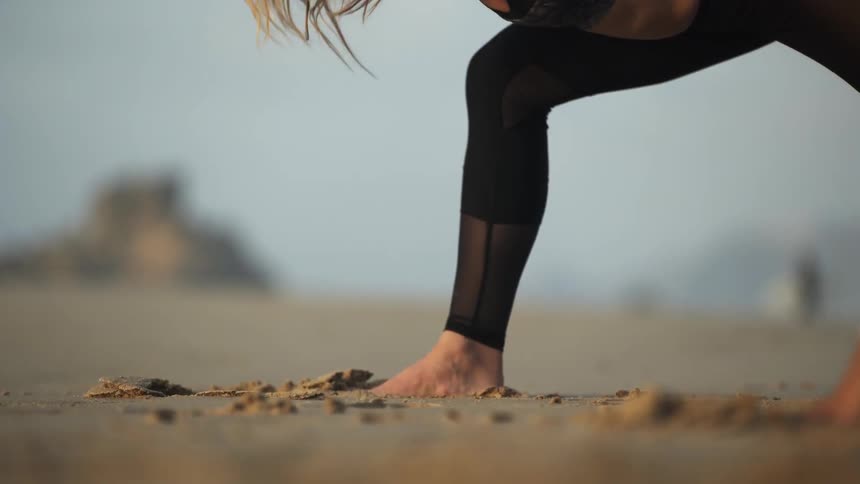 A woman is stretching leaning forward on the beach