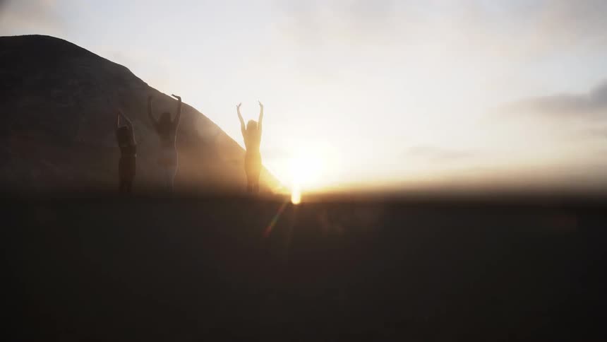 Three women are doing yoga on a beach at sunset