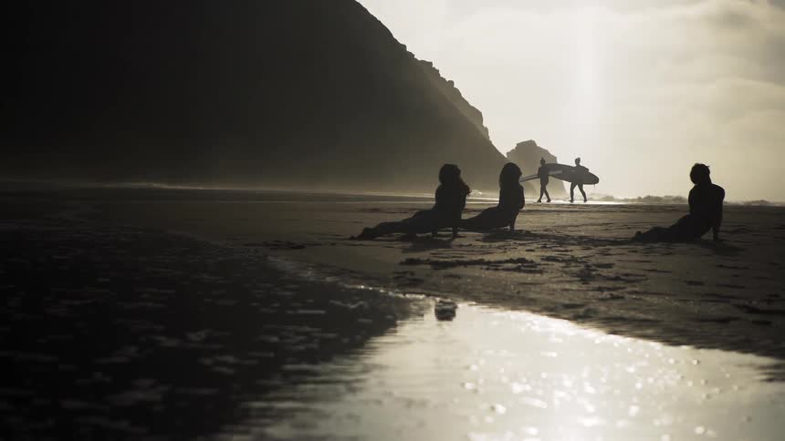 Women do yoga on a beach at sunset