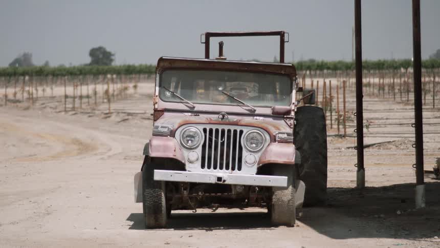 An old jeep parked on a sandy area with a large tire next to it