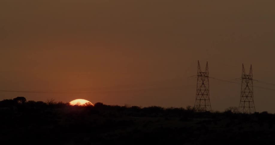 The sun is setting beyond power lines