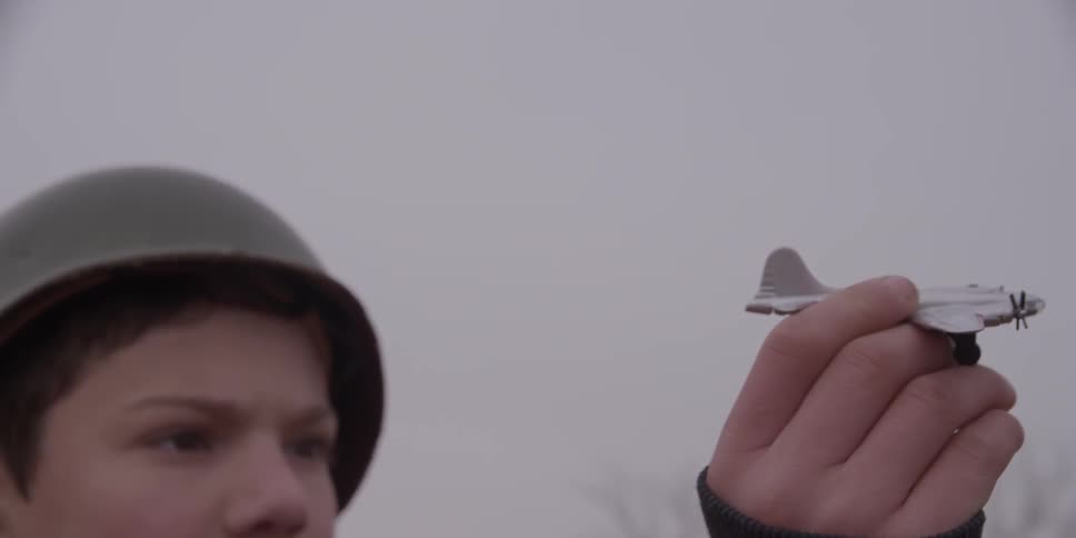 A boy wearing a helmet and holding a toy airplane pretending that it is flying