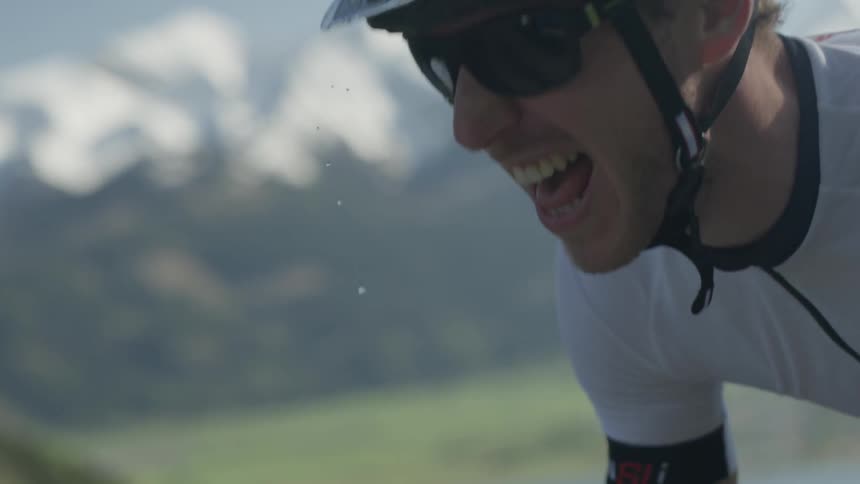 A man is breathing hard as he bikes on a mountain road in daylight