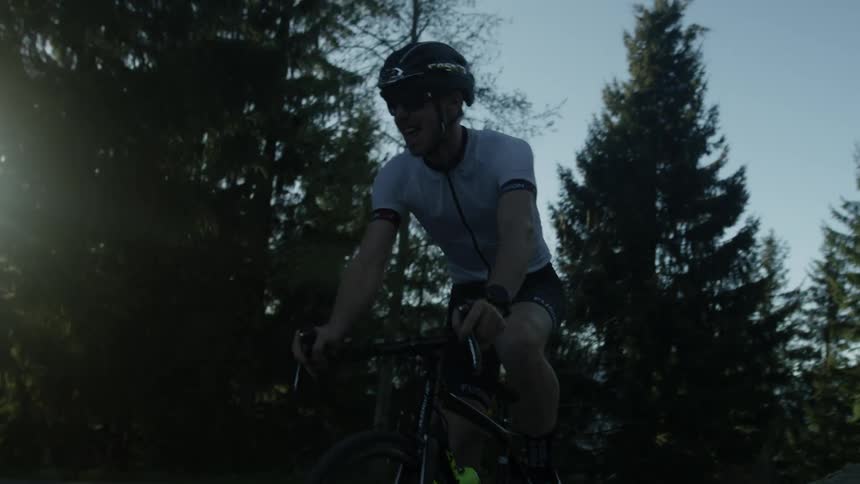 A man is bicycling on a road in a forest in daylight