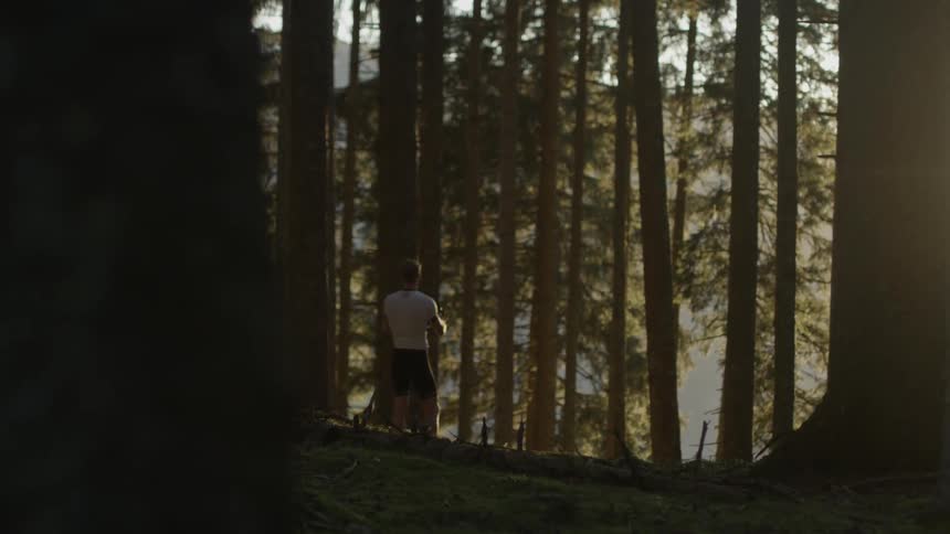 A bicyclist takes off his helmet in a forest