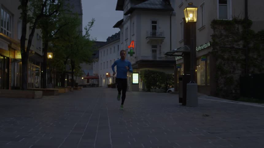 A man is jogging through a european city at dusk