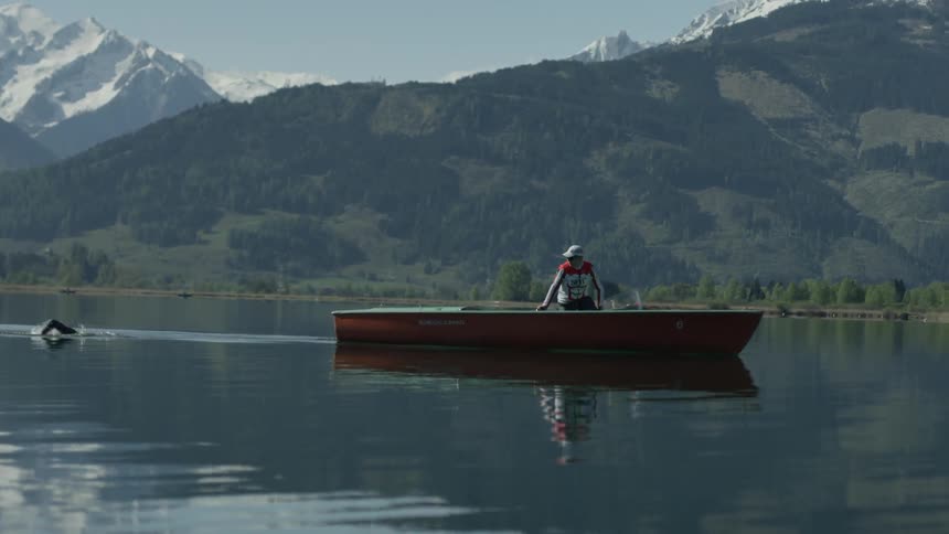 A boat is leading a swimmer as he swims in a mountain lake in daylight