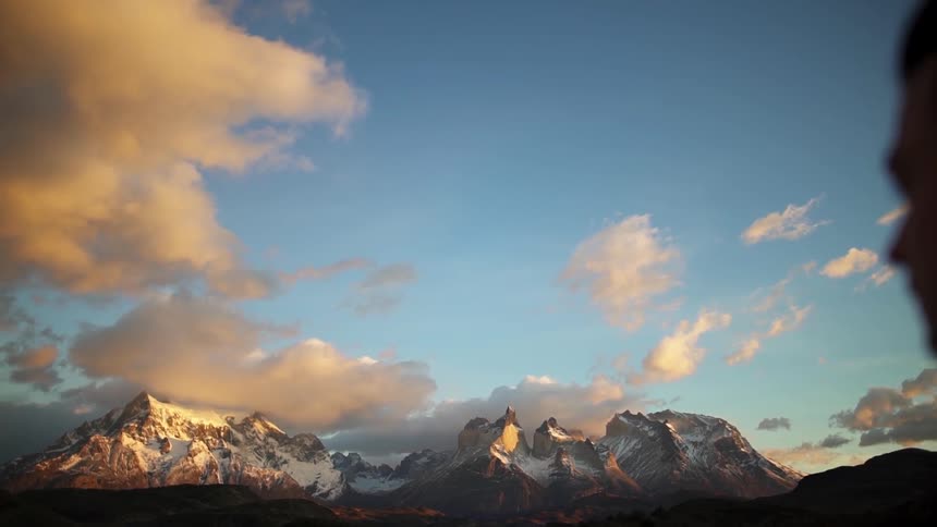 A man stands outside with snowy mountains in the distance