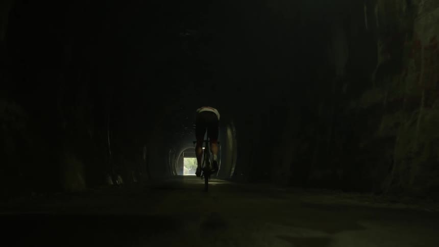 A man is riding his bike down the dark tunnel