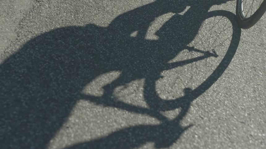 A person riding a bicycle is casting a shadow on the ground in daylight