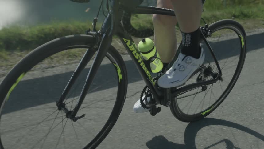 A man is pedaling a bicycle on a road on a sunny day