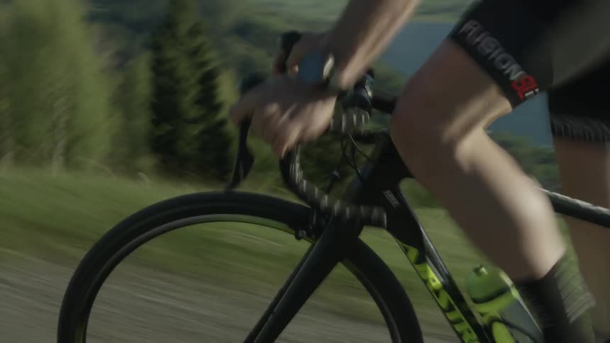 A man is pedaling a bicycle rapidly in a mountain landscape on a sunny day