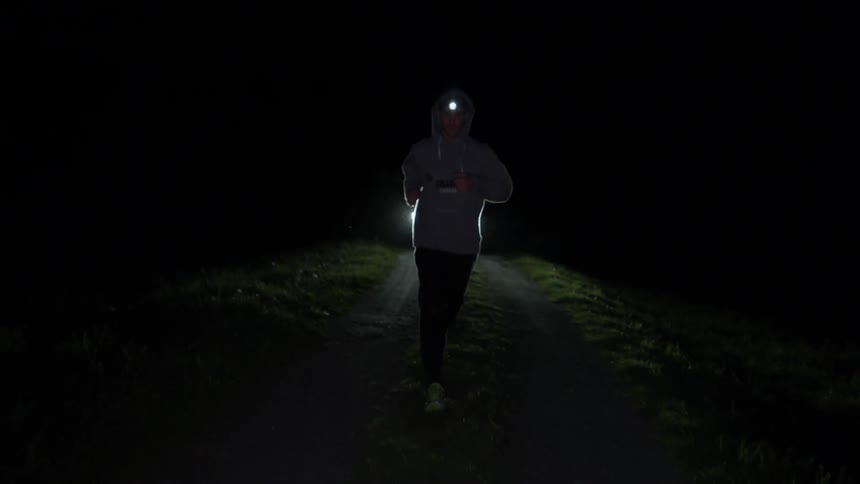 A man jogs in front of a car on a rural road at night