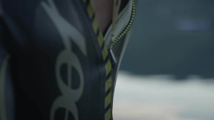 A man zips up a wet suit next to a lake