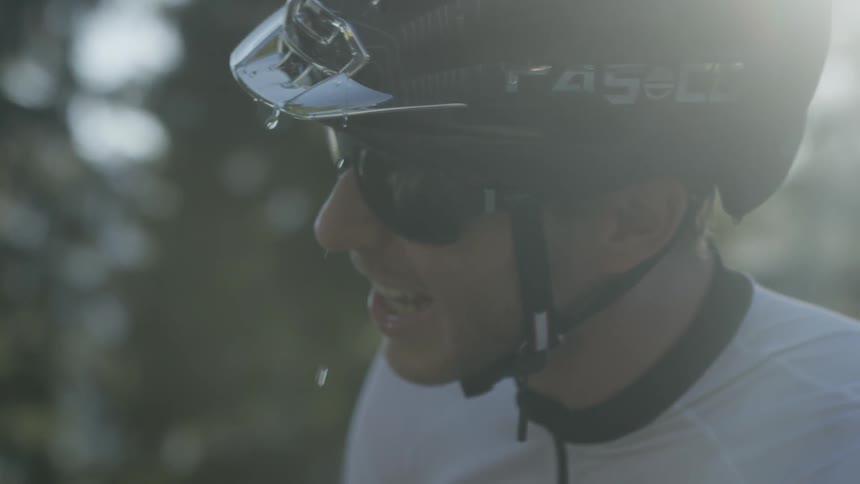 A man wearing a bicycle helmet drinks water then pours it on his head