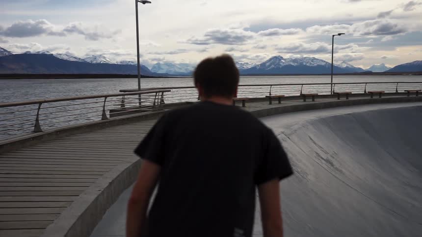 A man skateboards next to a mountain lake
