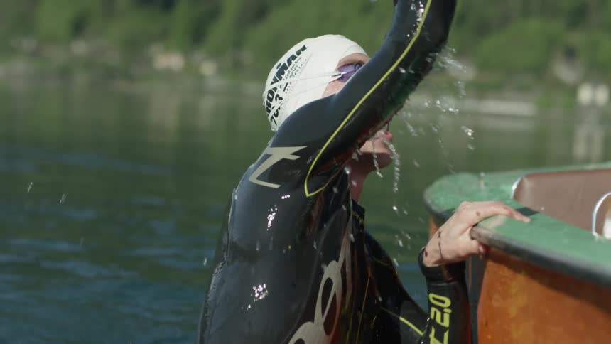A man is wearing a wetsuit and a swimming cap leaps from the water to high five someone