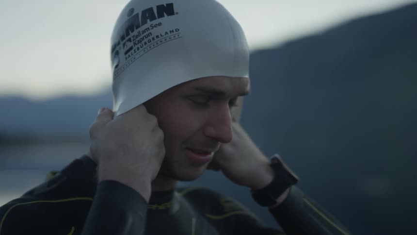 A man puts on a swim cap with water and mountains in the background