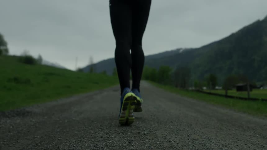 A man is jogging on a dirt trail under cloudy skies