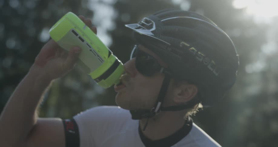 A male bicyclist is taking a drink from a water bottle outside in daylight