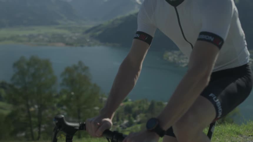 Man pedals bike on a high road near a lake and mountains
