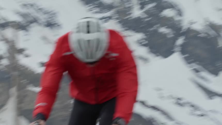 A man is pedaling a bicycle rapidly in a mountain landscape in daylight