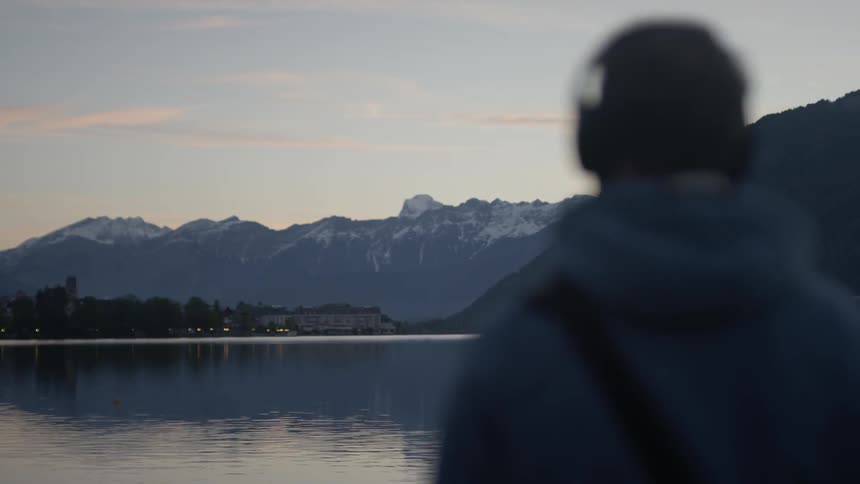 A man with headphones on stands and looks at the lake