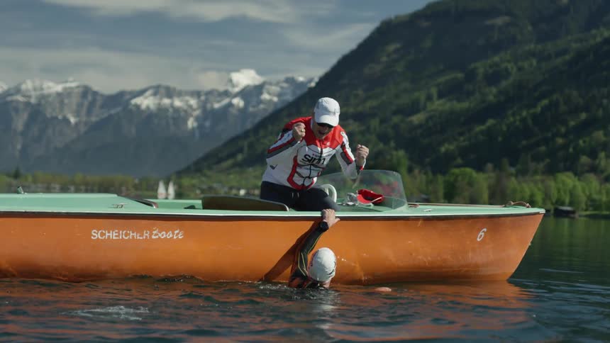 Man in the water holding onto a boat gives a high five to a man sitting in the boat