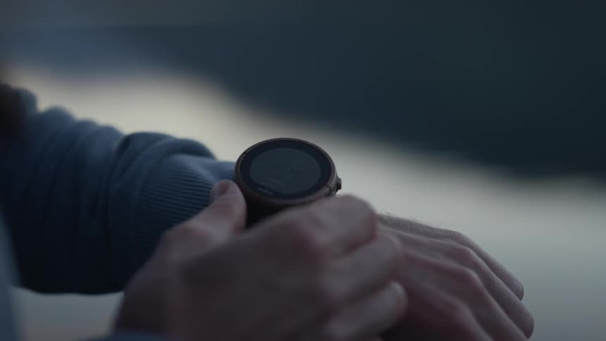 A man is clicking knobs on a stopwatch outside at dusk