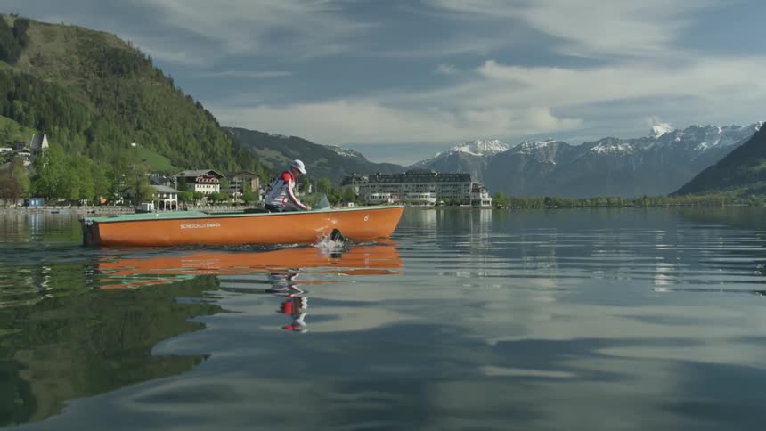 Person swims alongside small orange canoe in a river