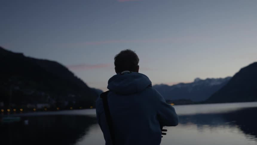 A man removes his hood while looking over the lake