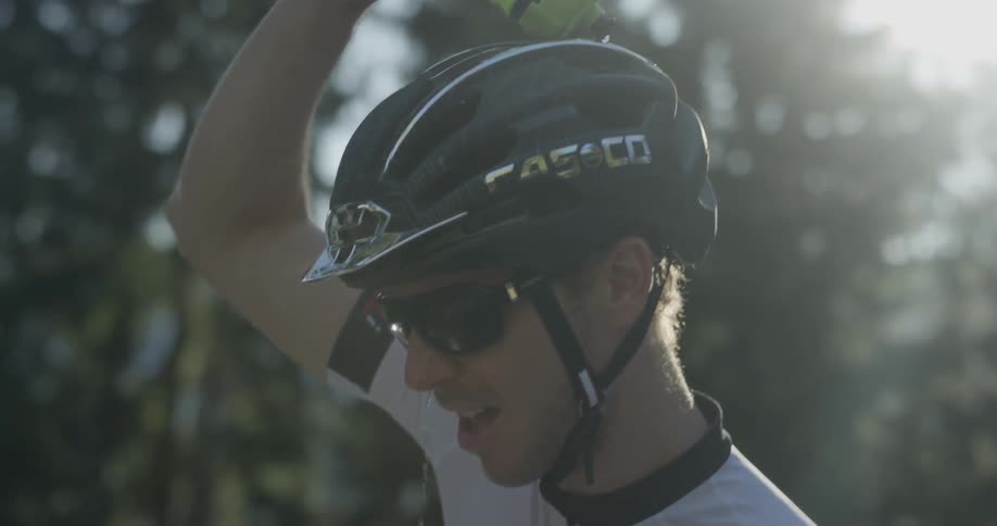 Man wearing a bike helmet pours water on his head in the woods on a sunny day