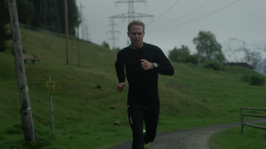 A man is running down a curved trail near a hill