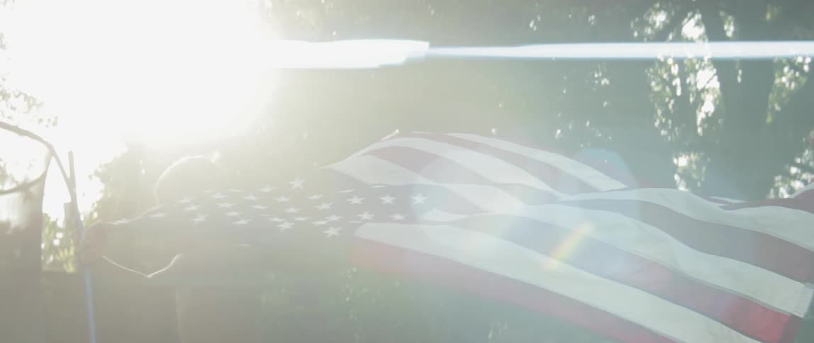 A boy is carrying a us flag as he runs in a backyard in daylight