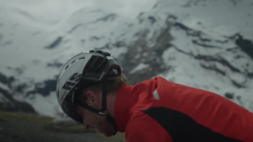 A man wearing a helmet rides a bike with a snow covered mountain in the background