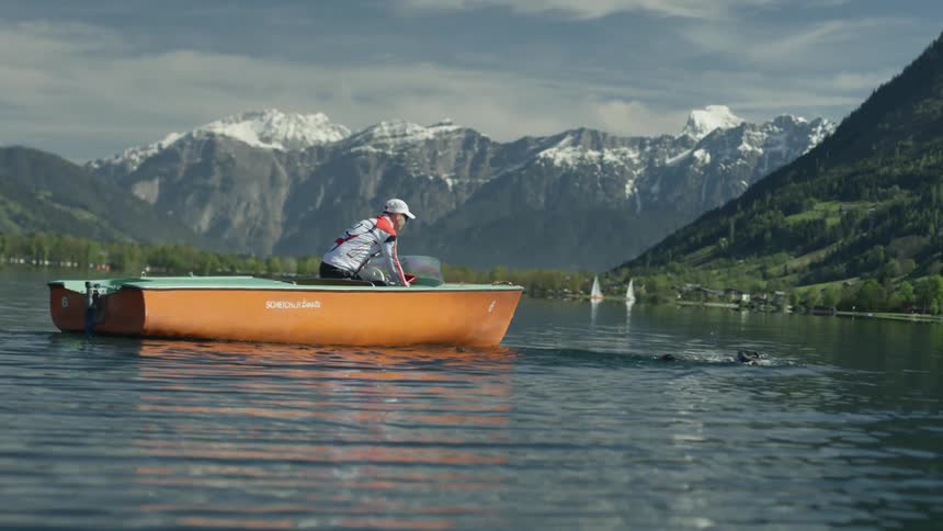 A man in a boat watches a swimmer in the water