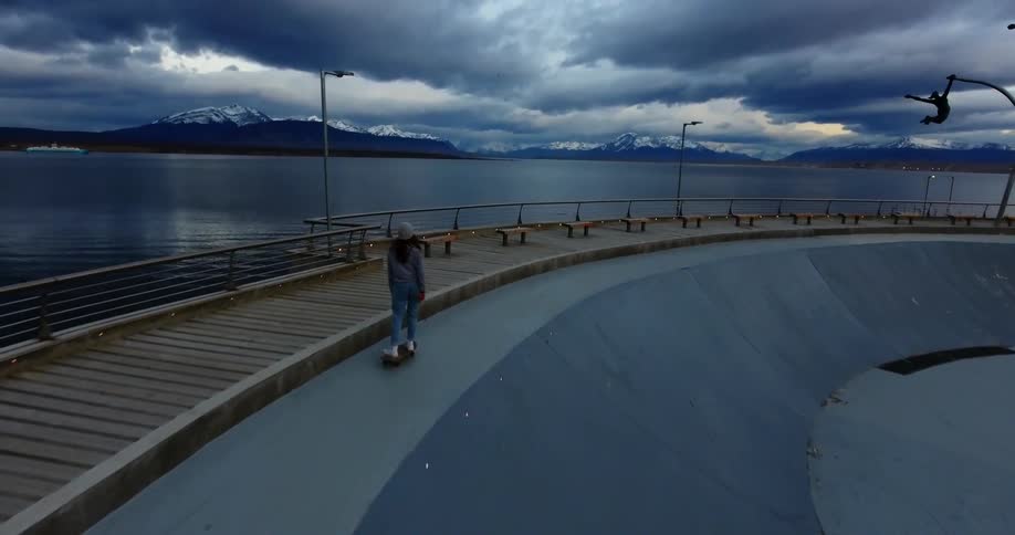 A skateboarder rides next to a mountain lake