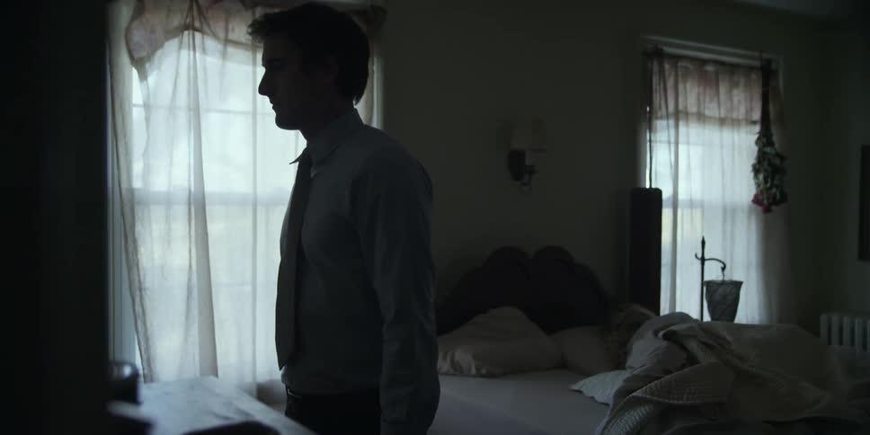 Man fixing his clothes as a person sleeps on the bed
